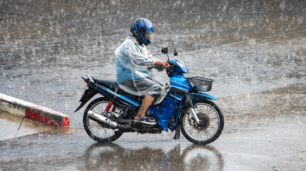 A motorcycle taxi driver rides in a heavy rain on a motorcycle