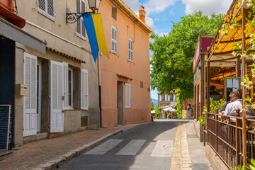 A narrow street with shops and a sidewalk cafe in the medieval hill town of Grimaud, France, above the town of Saint-Tropez and the French Riviera, Cote d'Azur.