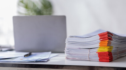 Stack of documents placed on a business desk and laptop in a business office.