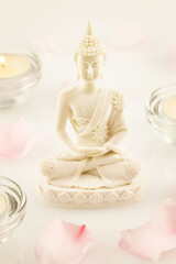Vesak, Buddha Day holiday, vertical card. Buddha statue, blurry rose petals and candles on a white background. Buddhism. Soft image and soft focus style