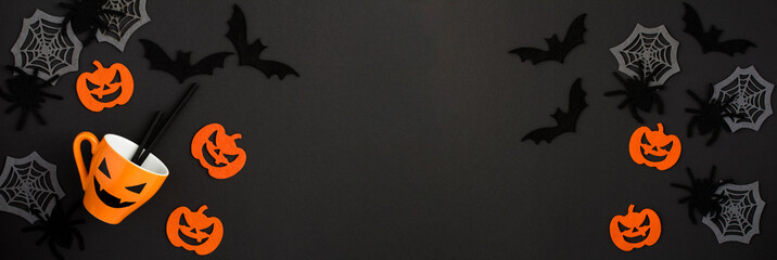 Halloween background. Orange cup, decorative spiders, pumpkins, spider webs and bats on the black background. Copy space. Top view.