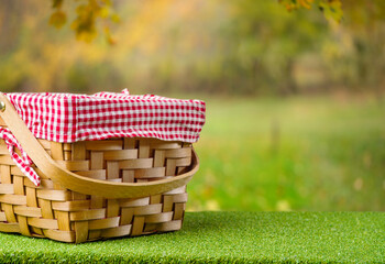On a green lawn, a straw picnic basket against the backdrop of a picturesque autumn nature. Family traditions, thanksgiving and harvest day celebrations, outdoor activities. - 521497104