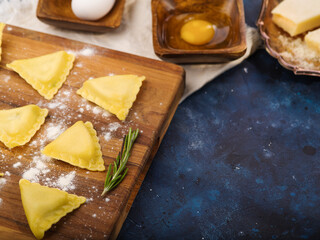 Appetizing ravioli on a cutting board and ingredients on a blue marble background. Italian cuisine...