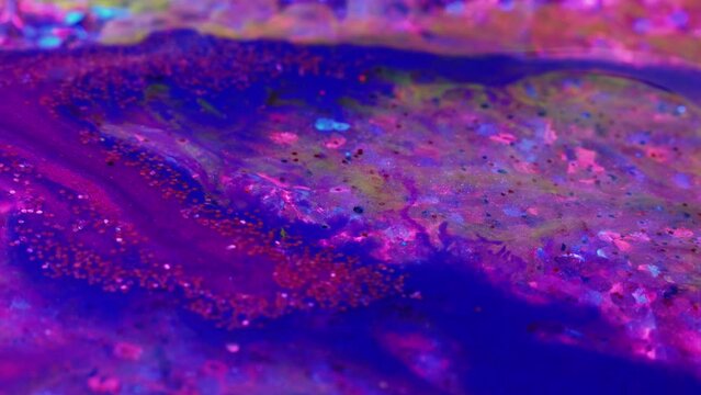 Creative art. Fluid magic. Painting process. Purple and blue glittered stream of liquid paint floating and mixing together in macro shooting.