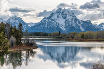 Fototapeta na wymiar River surrounded by Trees and Mountains in American Landscape. Snake River, Oxbow Bend. Spring Season Sunset. Grand Teton National Park. Wyoming, United States. Nature Background.