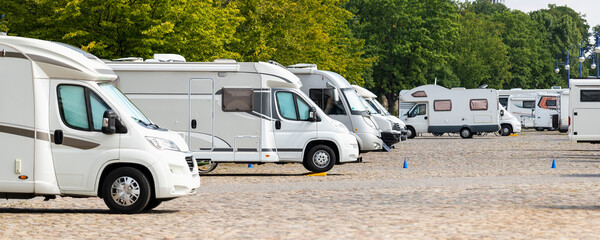 Many white modern campervan recreational motor home vehicles parked in row at camper park site...