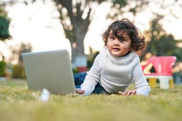 Smart little boy playing at garden while using laptop on meadow,home insurance concept.