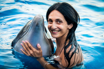 Portrait of young Caucasian woman smile with dolphin look to camera in pool water of Batumi delphinarium. Swim with dolphin experience concept - Powered by Adobe