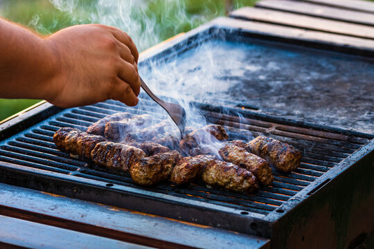 Preparing meat rolls called mici or mititei on barbecue. close up of grill with burning fire with flame and smoke.