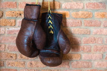 A pair of vintage boxer leather gloves hang against a brick wall. Retro style.	