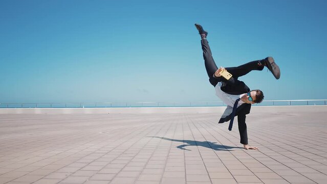 Flexible and cool businessman doing acrobatic tricks outdoor. Young business man having fun dancing while going to work.