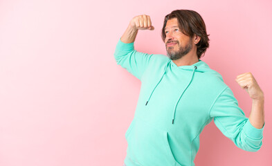 Senior dutch man isolated on pink background doing strong gesture