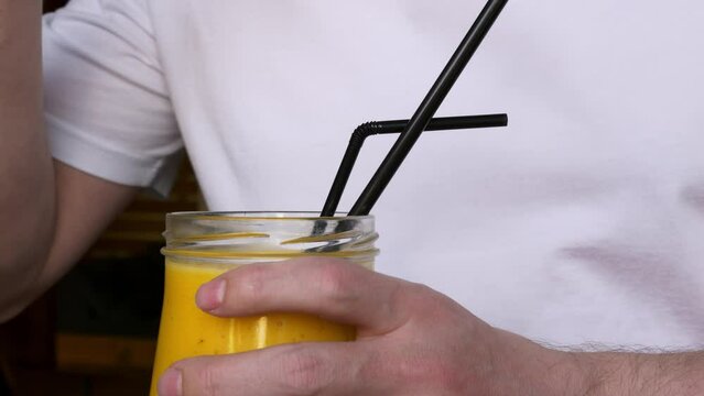 Close-up shot of a full glass of smoothie, from a glass cup eat a yellow mango smoothie with a spoon. Consumption of vitamins from fresh fruits to maintain good health and mood.