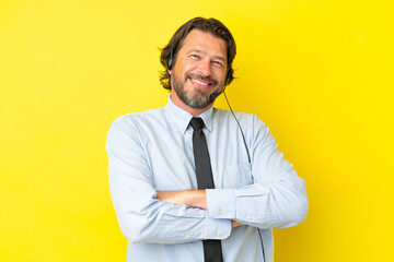 Telemarketer dutch man working with a headset isolated on yellow background keeping the arms...