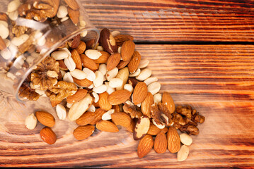 A mixture of different nuts is poured from a glass jar onto the table