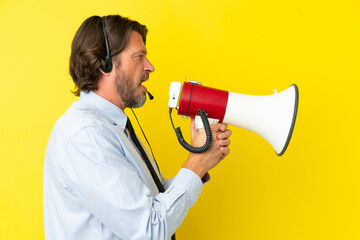 Telemarketer dutch man working with a headset isolated on yellow background shouting through a megaphone