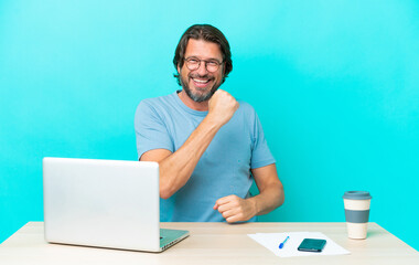 Senior dutch man in a table with a laptop isolated on blue background celebrating a victory