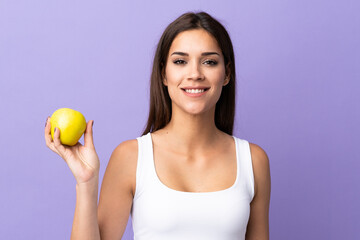 Young caucasian woman isolated on purple background with an apple and happy
