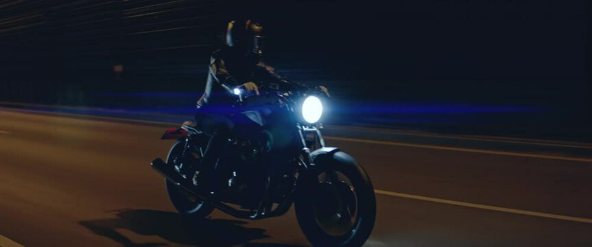 TRACKING Shot of a biker riding his custom built cafe racer motorcycle through city at night. Shot with 2x anamorphic lens