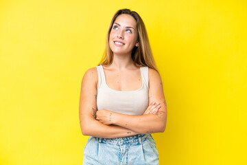 Young caucasian woman isolated on yellow background looking up while smiling