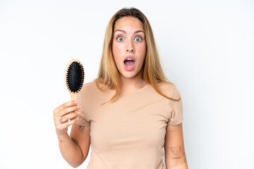 Young caucasian woman with hair comb isolated on white background with surprise and shocked facial expression
