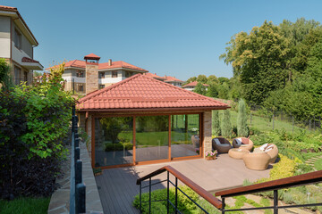 Beautiful covered terrace with large glass windows in the summer garden.