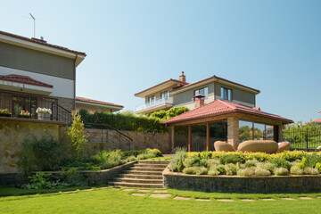 View of the terrace of a modern house in the garden. Large glass windows, brown roof. Cozy patio with wicker furniture.