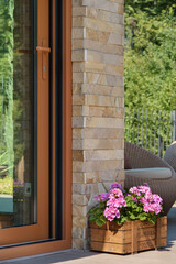 Glass door to the terrace of a country house. Wooden box with flowers. Wicker garden furniture.