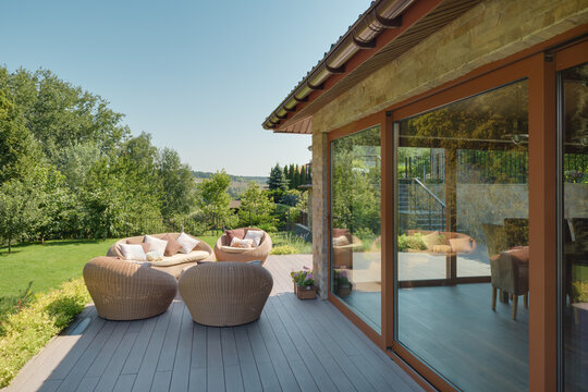 Garden terrace made of glass and stone. Large glass windows, wooden floor and wicker garden furniture.