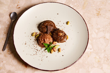 Scoops of healthy raw vegan chocolate sorbet topped with pistachio, lemon basil on a serving plate on marble background.