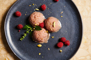 Scoops of healthy raw vegan sorbet topped with raspberries, pistachio, lemon basil on serving plate on marble background