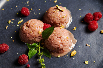 Scoops of raspberry sorbet with sprinkled green pistachio nuts, raspberries and lemon basil on dark blue plate. Close-up
