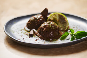 Scoops of chocolate sorbet, with sprinkled matcha powder, slice of lime, lemon basil on dark blue plate. Selective focus