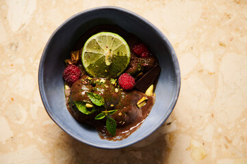 Selective focus on slice of juicy lime, garnishing raspberry chocolate ice cream in navy blue bowl. Flat lay Still life