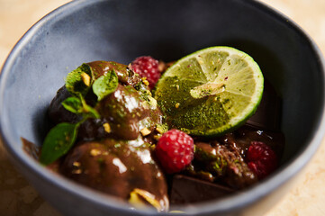 Selective focus on a slice of juicy lime, garnishing a raspberry chocolate ice cream in navy blue bowl. Food still life