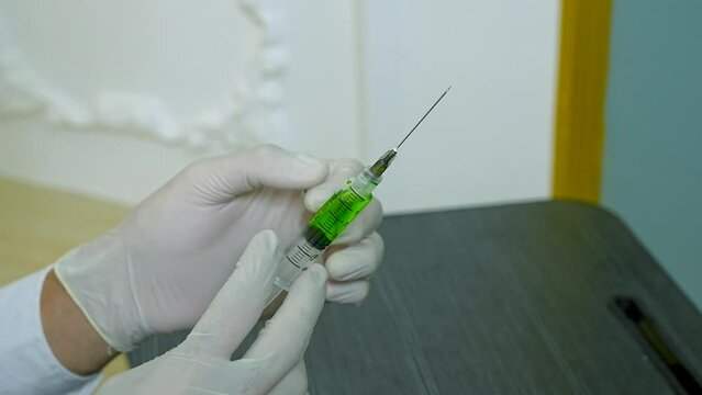 Young male nurse checking and knocking a syringe filled with green liquid