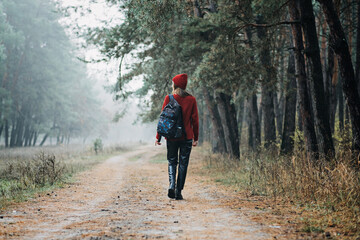 Fototapeta premium Weekend breaks and getaways in forests. Stay close to nature. Young woman in red hat and sweater with backpack