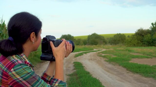 A young woman in a field photographs nature. A girl with a camera walks in nature. Camera movement towards the subject. The concept of happiness, hobby, relaxation.
