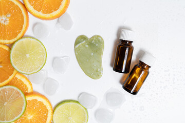 brown glass jars of oil and a guasha massager lie on a white background with ice and citruses in the form of lime and orange