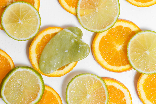 A Green Gouache Massager Lies On Round Slices Of Orange And Lime On A White Background Covered With Water Drops. Background For Your Design