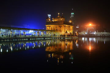 Fototapeta na wymiar Causeway to main Gurdwara of Golden Temple. Illuminated at night and reflecting in holy water.