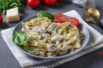 Tagliatelle pasta with chicken and cheese, served with cherry tomatoes and basil on gray background