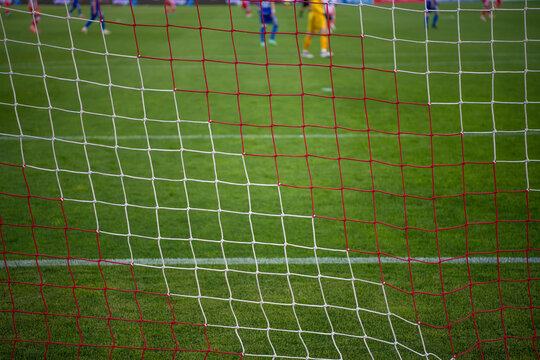 Football goal net during the game. Blurred players in background. Soccer background blurred photo, focus on net.
