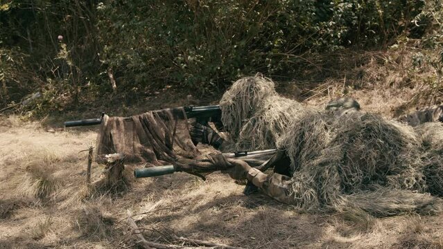 Snipers in an ambush in the grass, disguised as terrain on an anti-terrorist operation with sniper rifles, shooting at the enemy. Footage of military operations. Soldiers in full gear. Cinematic shot