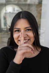 Fototapeta na wymiar face of a young woman with a finger in her mouth, silence gesture while smiling, latin person with long hair, natural beauty