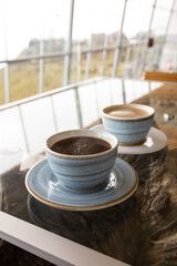 served table with cup of coffee and latte, light blue decorated crockery, hot drink in restaurant, caffeinated breakfast