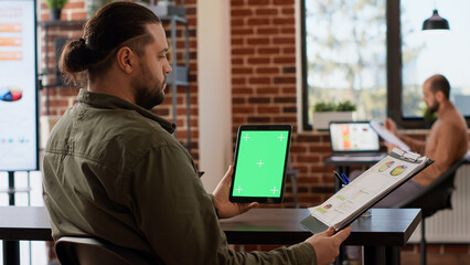 Male freelancer planning startup business with greenscreen on digital device at office job. Working on tablet display with isolated copyspace template and chroma key background.