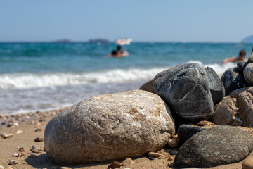 Natural stones on the beach, silhouettes of people swimming in the sea.