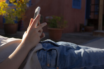 A teenage girl looks at her cell phone while lying in the garden at sunset. Unrecognizable person.