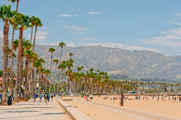 Santa Barbara beach promenade with walking people, sandy beach, and mountains and cloudy sky on...